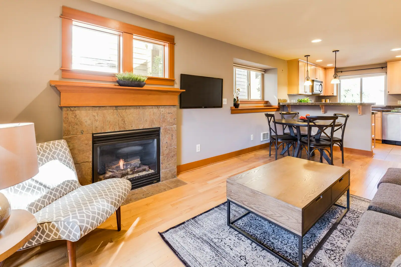 Open living room with a stone fireplace, wood floors and a kitchen beyond